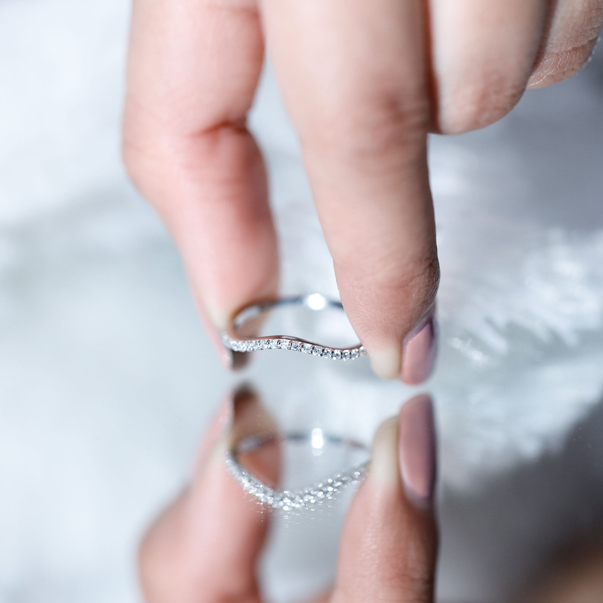 White gold curved diamond band held between fingers, showing a delicate chevron contour and slim pavé-set lab grown diamonds.