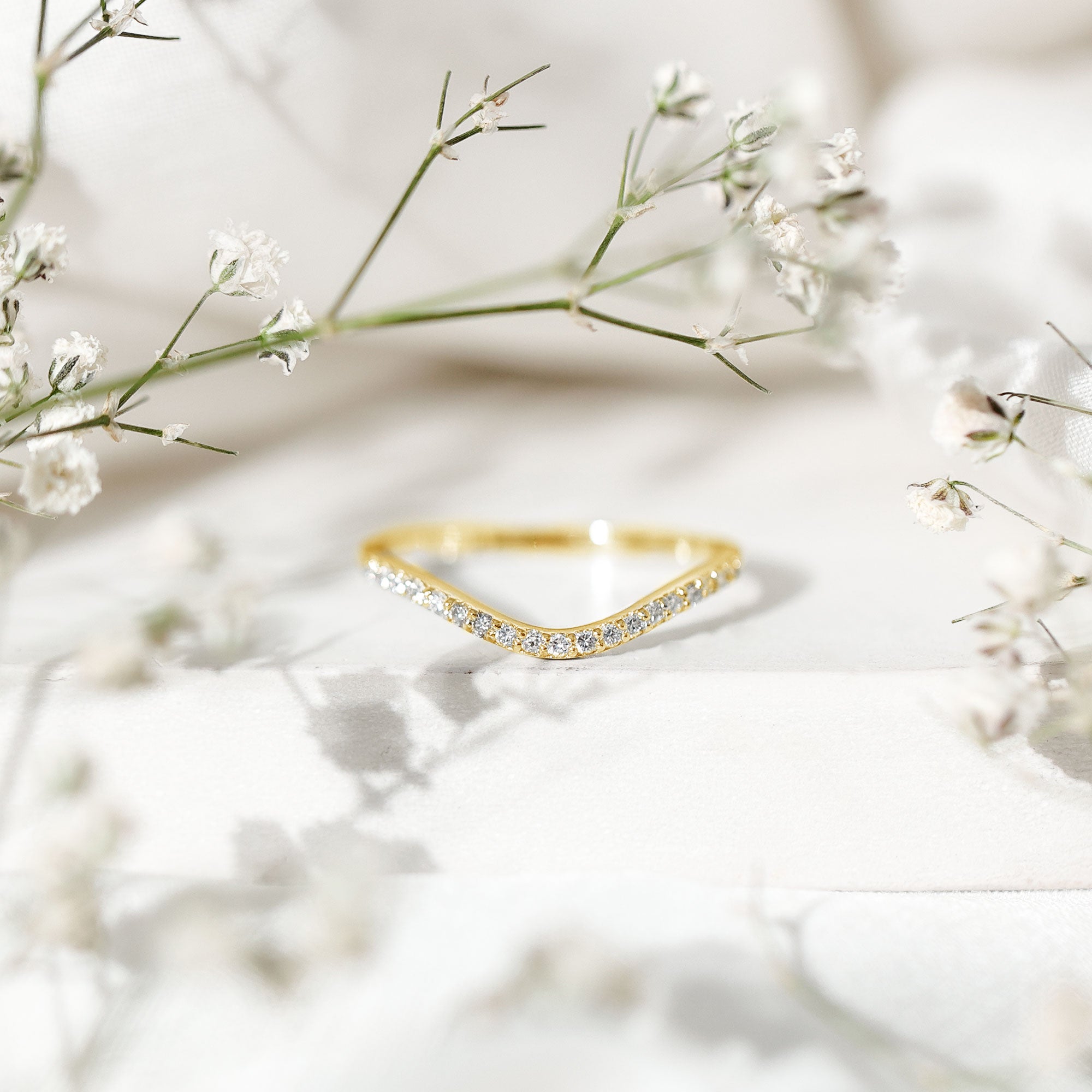 Yellow gold curved diamond wedding band displayed on a white pedestal with floral styling and a refined chevron shape.