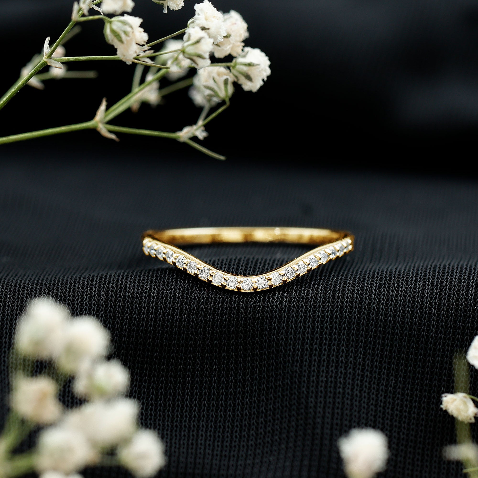 Yellow gold V-shaped lab grown diamond band styled on black fabric, showing a delicate contour wedding ring design.