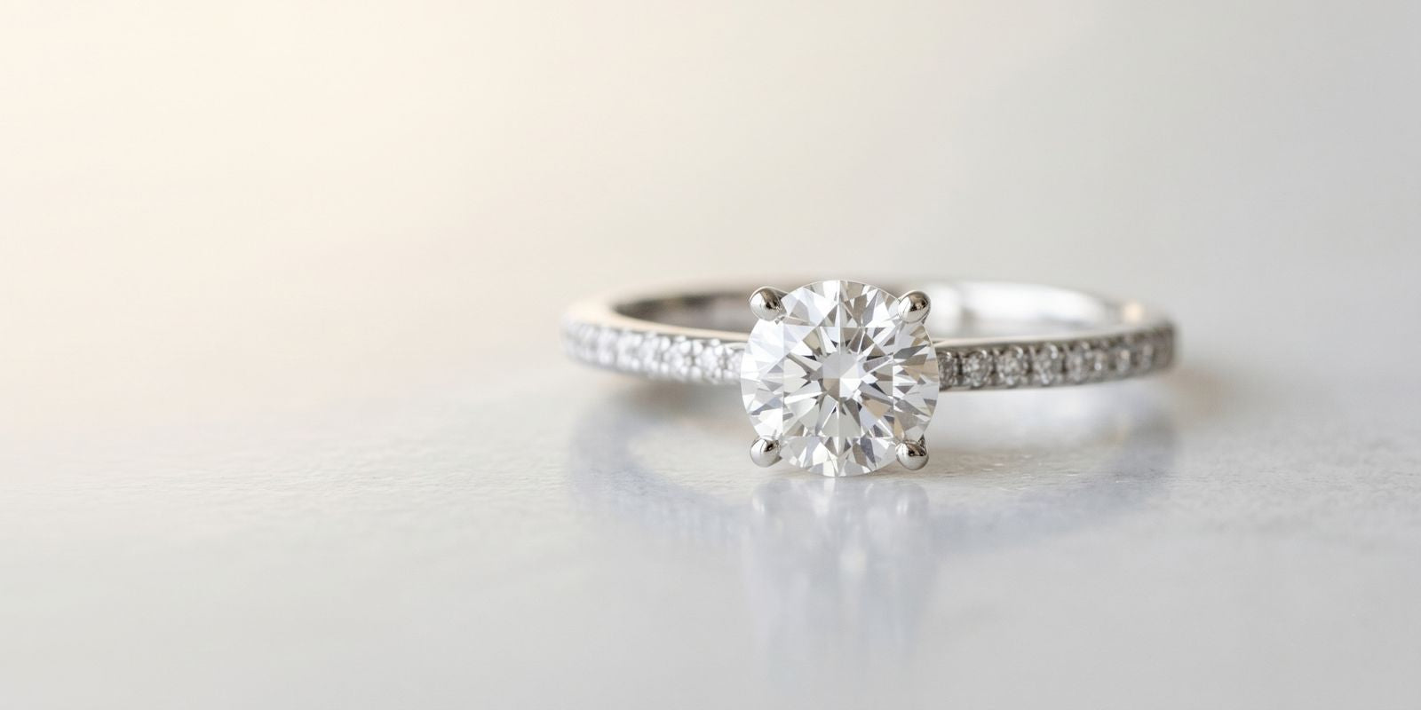 Close-up of an affordable lab grown diamond promise ring with an oval center stone and pavé band on a soft neutral background.