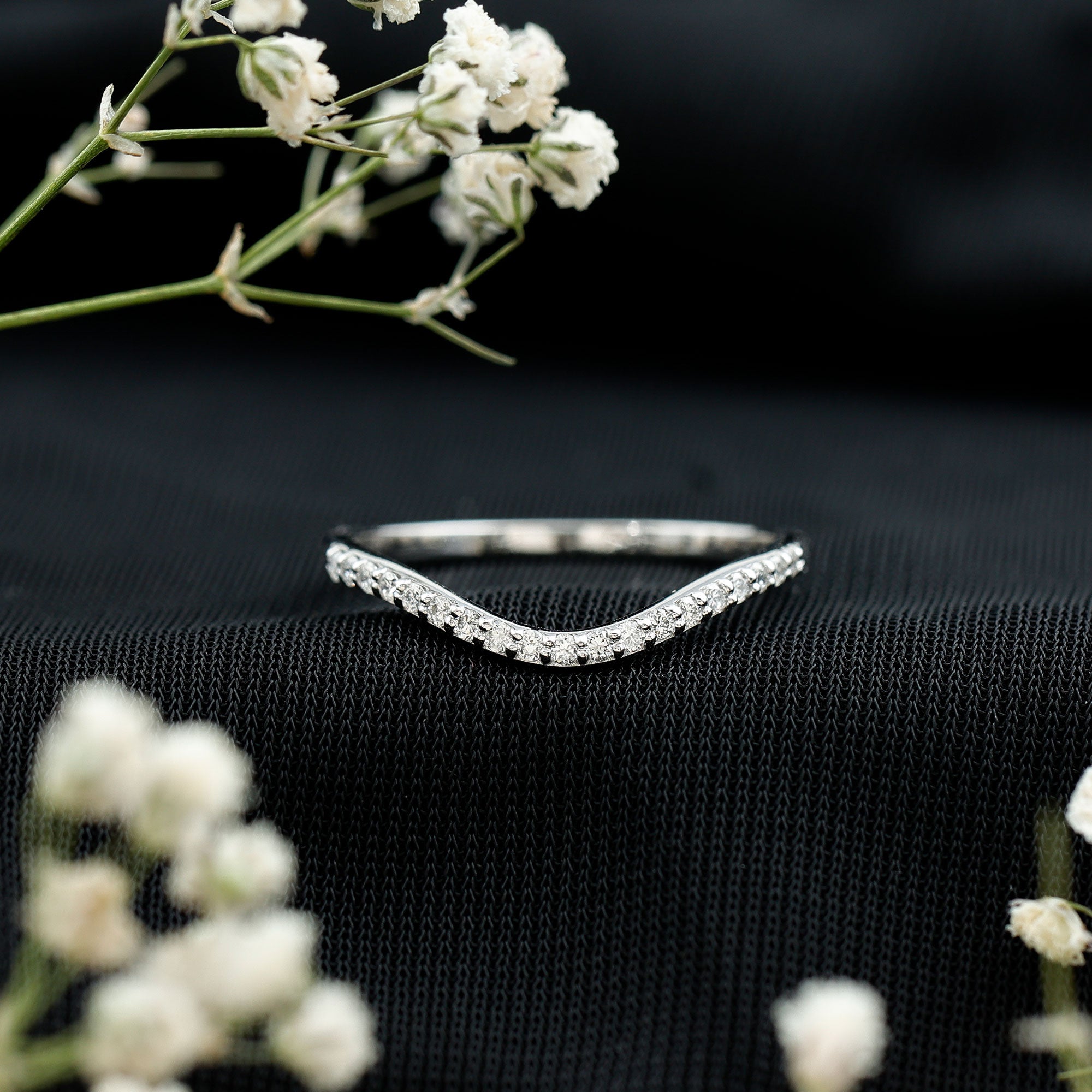 White gold V-shaped lab grown diamond wedding band styled upright on black fabric with floral accents.